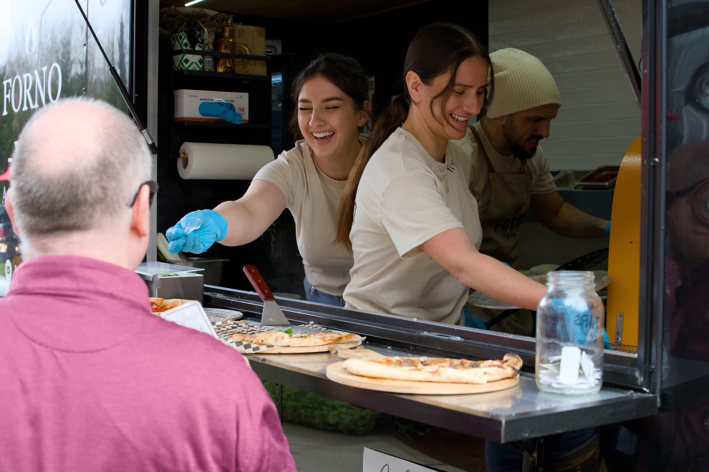 Forno Via team serving fresh pizza to guests from the trailer