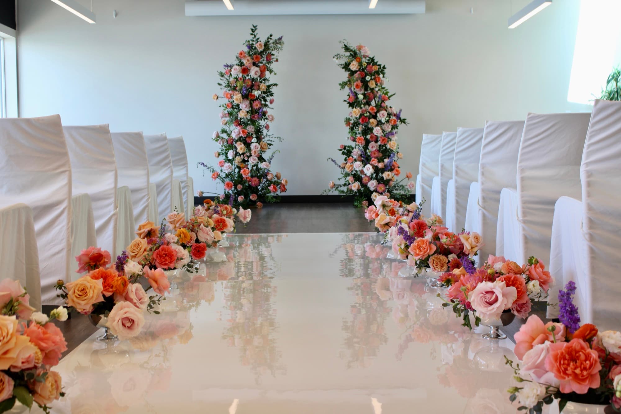 A symmetrical wedding ceremony aisle with peach and coral floral pedestals designed by Events by Juna.